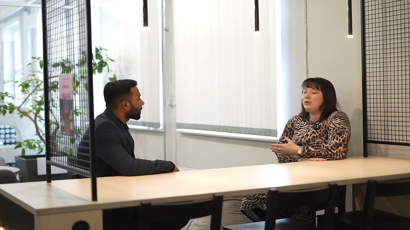 An EKA representative and our CEO seated across a long shared table in an EKA study area, with mesh partitions and pendant lights behind them