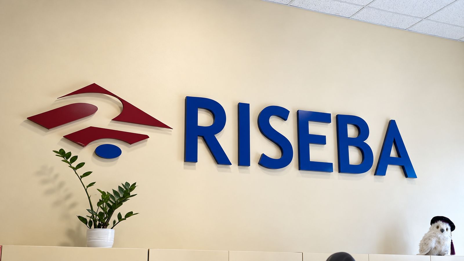 RISEBA's logo and name in large letters on its reception wall, beside a potted plant