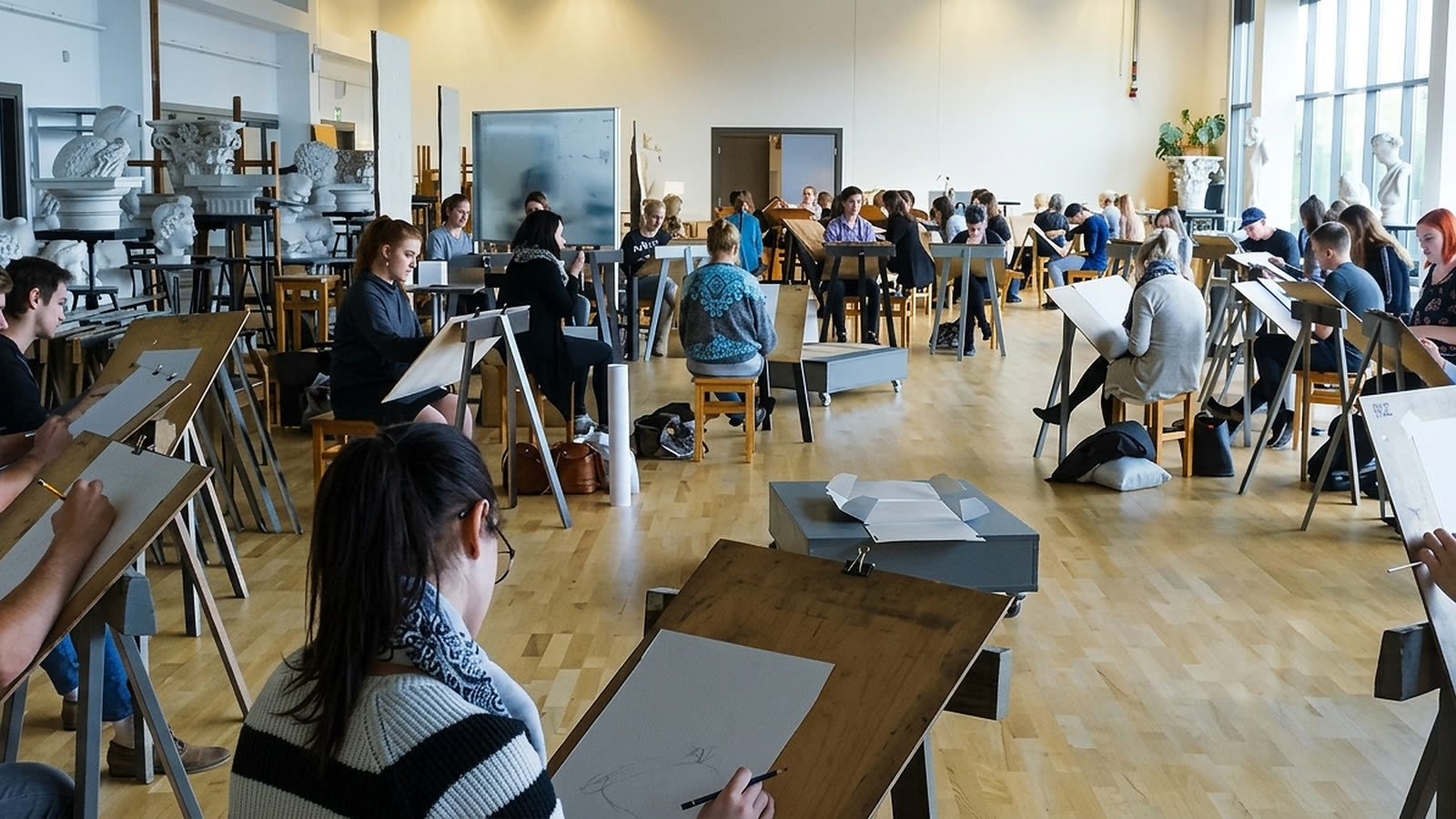 Students drawing at easels in a bright studio at RTU, with plaster busts on the shelves