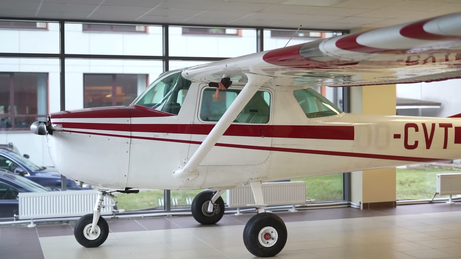 A red-and-white light aircraft on display inside a glass-walled hall at TSI