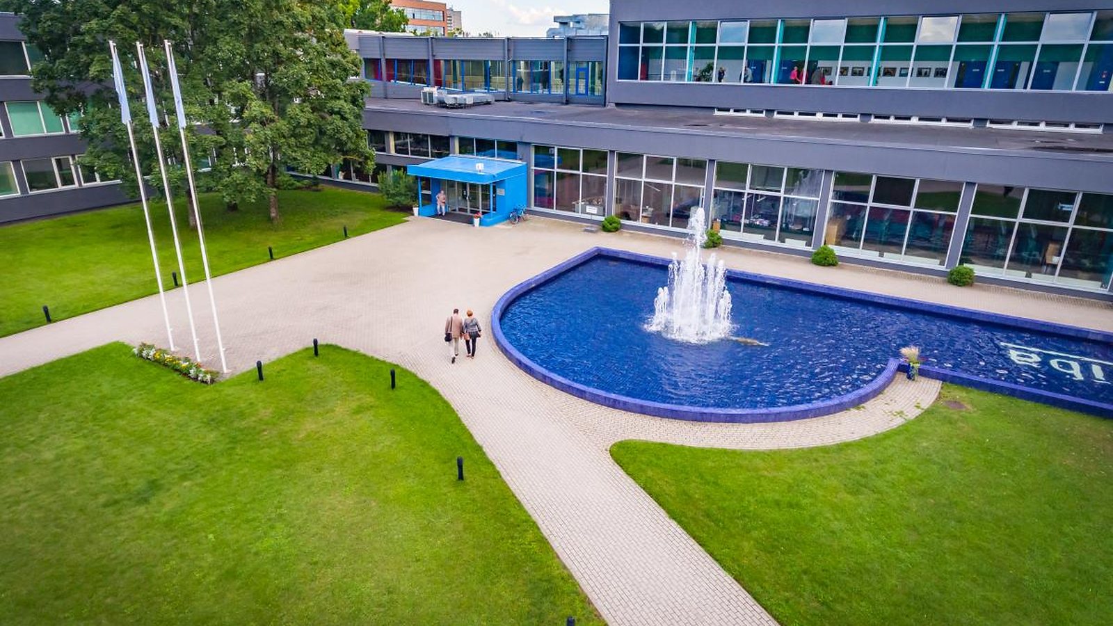 Turība's main building in Riga from above: a long glass front, three flagpoles and a blue fountain pool in the forecourt