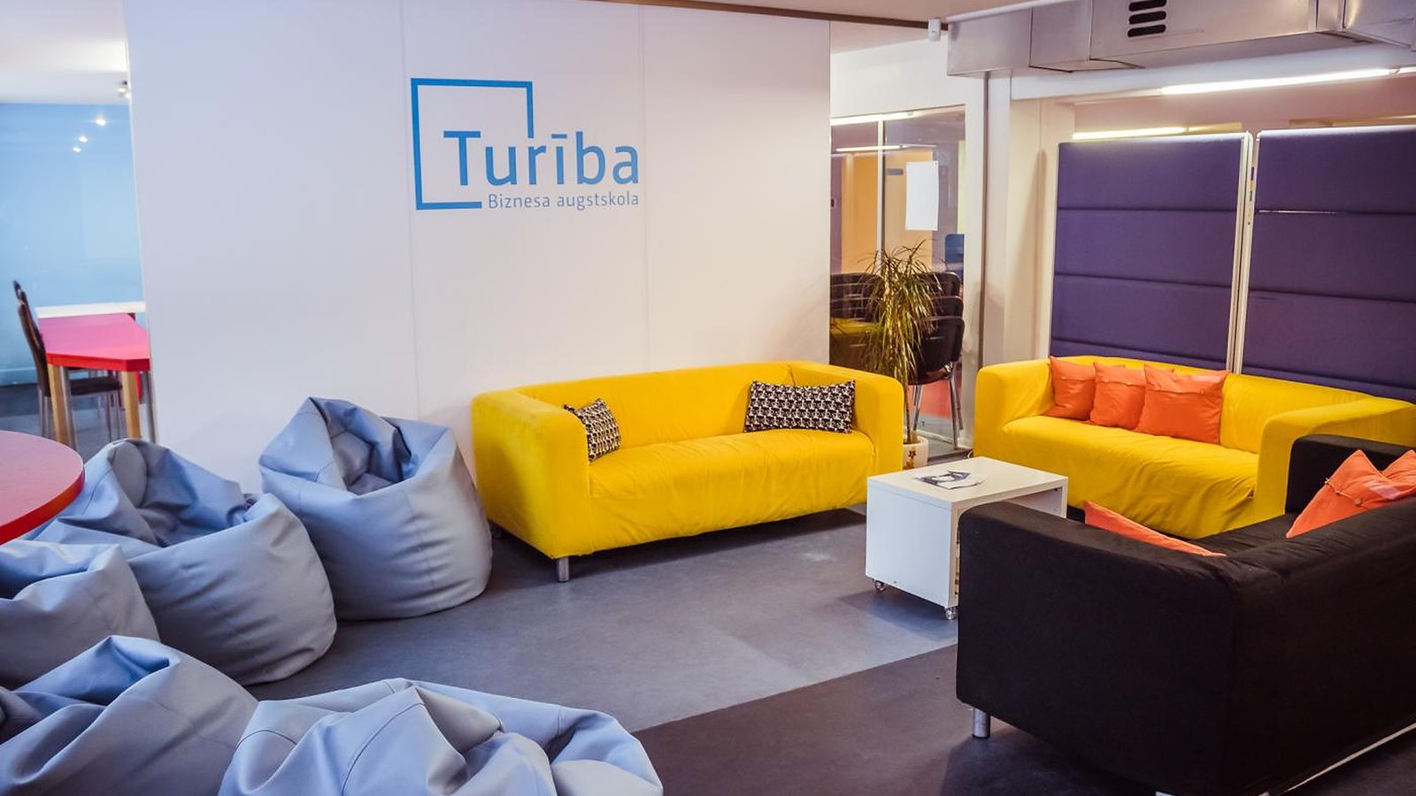 A student lounge at Turība with yellow sofas and bean bags, the Turība logo on the wall