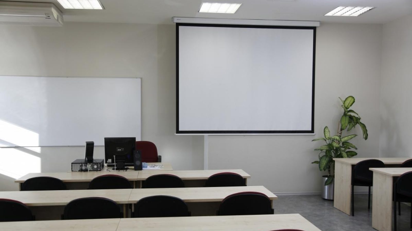 A lecture room at Turība with a projection screen, a whiteboard and rows of desks